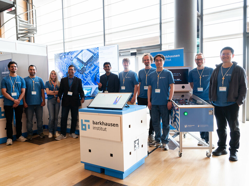 Group of people standing behind a display booth with 'barkhausen institut' signage in a modern indoor setting