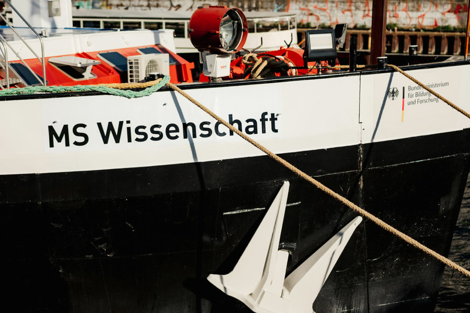 Bildausschnitt der Seite des Wissenschaftsschiffes MS Wissenschaft. Man sieht den Schriftzug "MS Wissenschaft", die leinen, die das Schiff halten und einige schiffstypische Elemente an Bord.