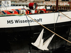Bildausschnitt der Seite des Wissenschaftsschiffes MS Wissenschaft. Man sieht den Schriftzug "MS Wissenschaft", die leinen, die das Schiff halten und einige schiffstypische Elemente an Bord.