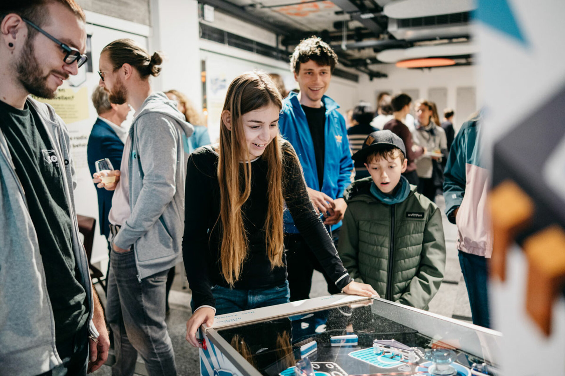 Several people playing a pinball machine at the opening of the exhibition 'Mensch, Roboter! – Robotik aus der Dresdner Wissenschaft' in a bright room.