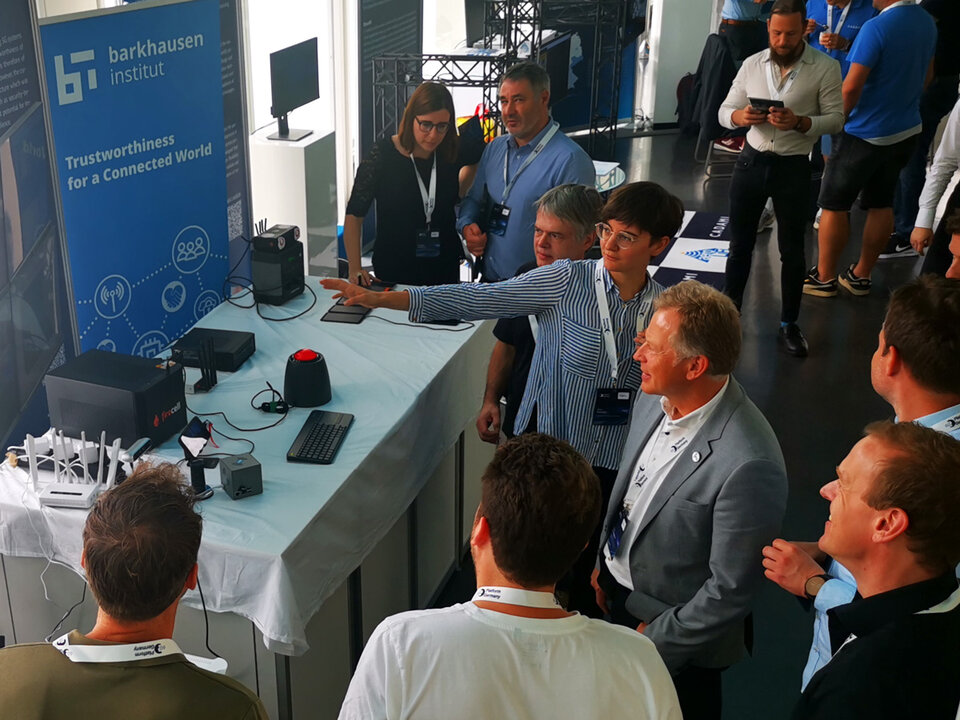 Mehrere Personen stehen an einem Messestand mit einem Banner des Barkhausen Instituts und technischen Geräten auf einem Tisch