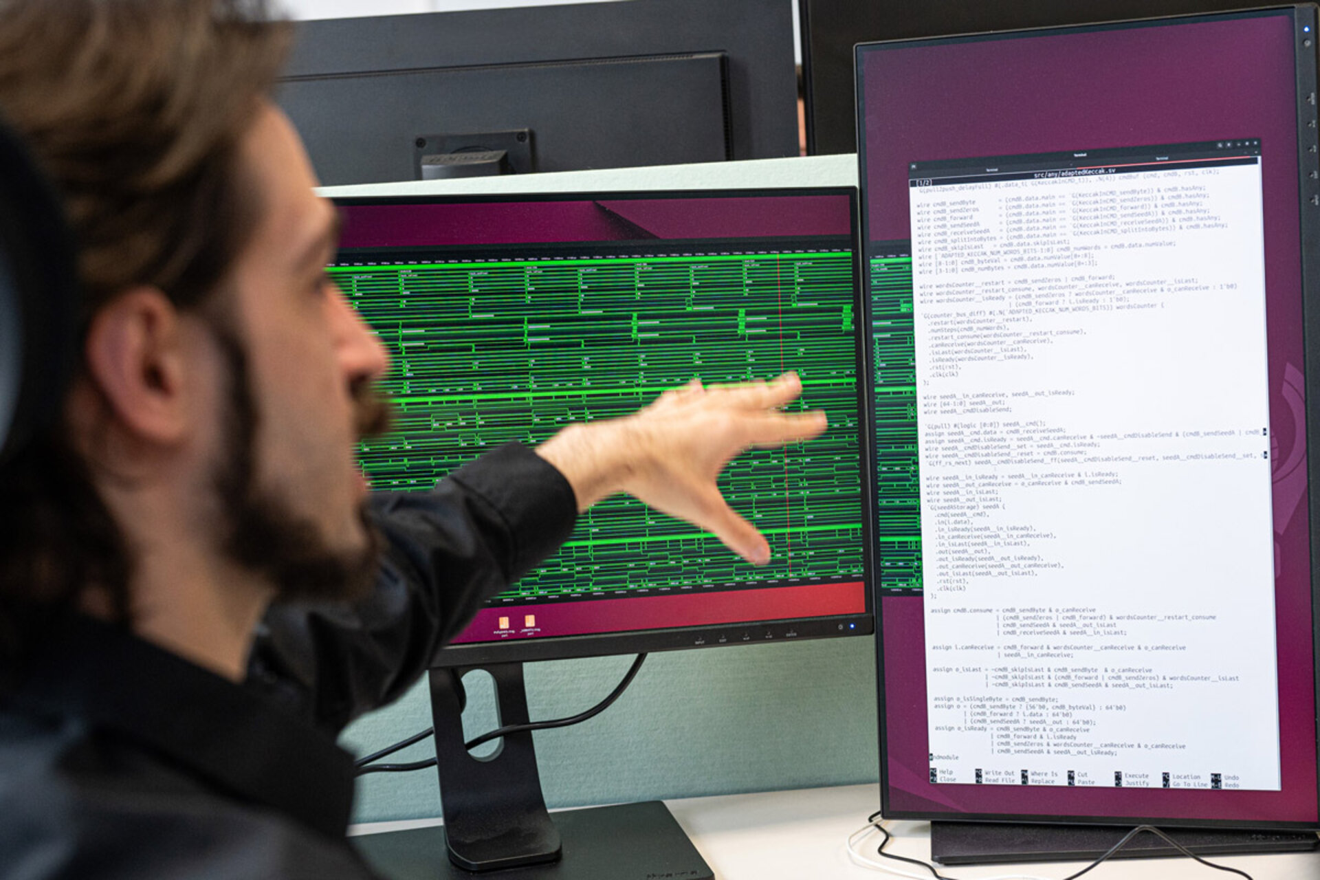 Person pointing at two computer monitors displaying code and data visualizations