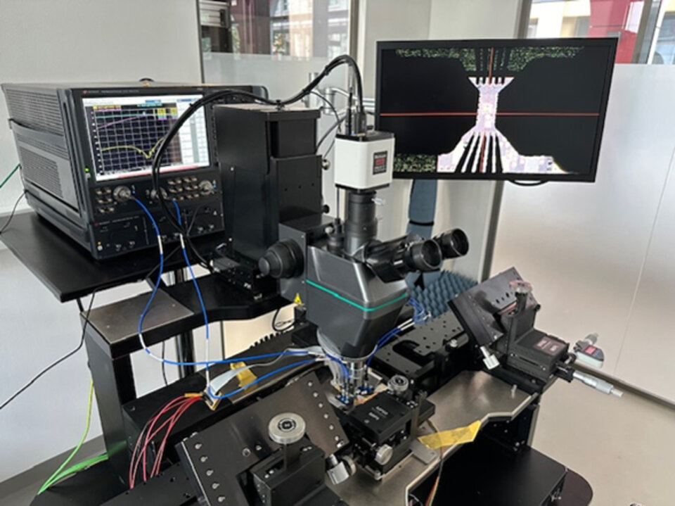 Mikroskopaufbau mit mehreren angeschlossenen Geräten und einem Monitor, der ein vergrößertes Bild einer Mikrostruktur anzeigt