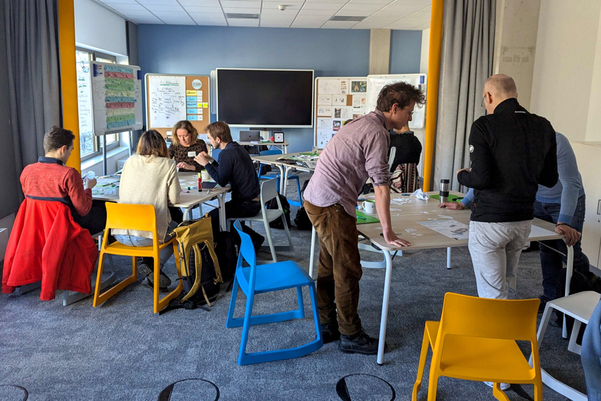 Workshop 'Besser visualisieren' with participants at tables, some standing and others sitting. Various materials and notes on the tables.