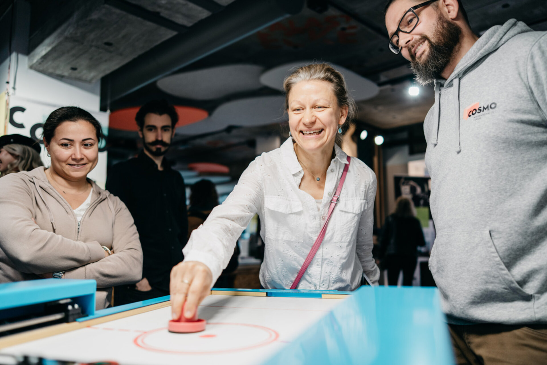 Person in white shirt playing air hockey surrounded by others in an exhibition space.