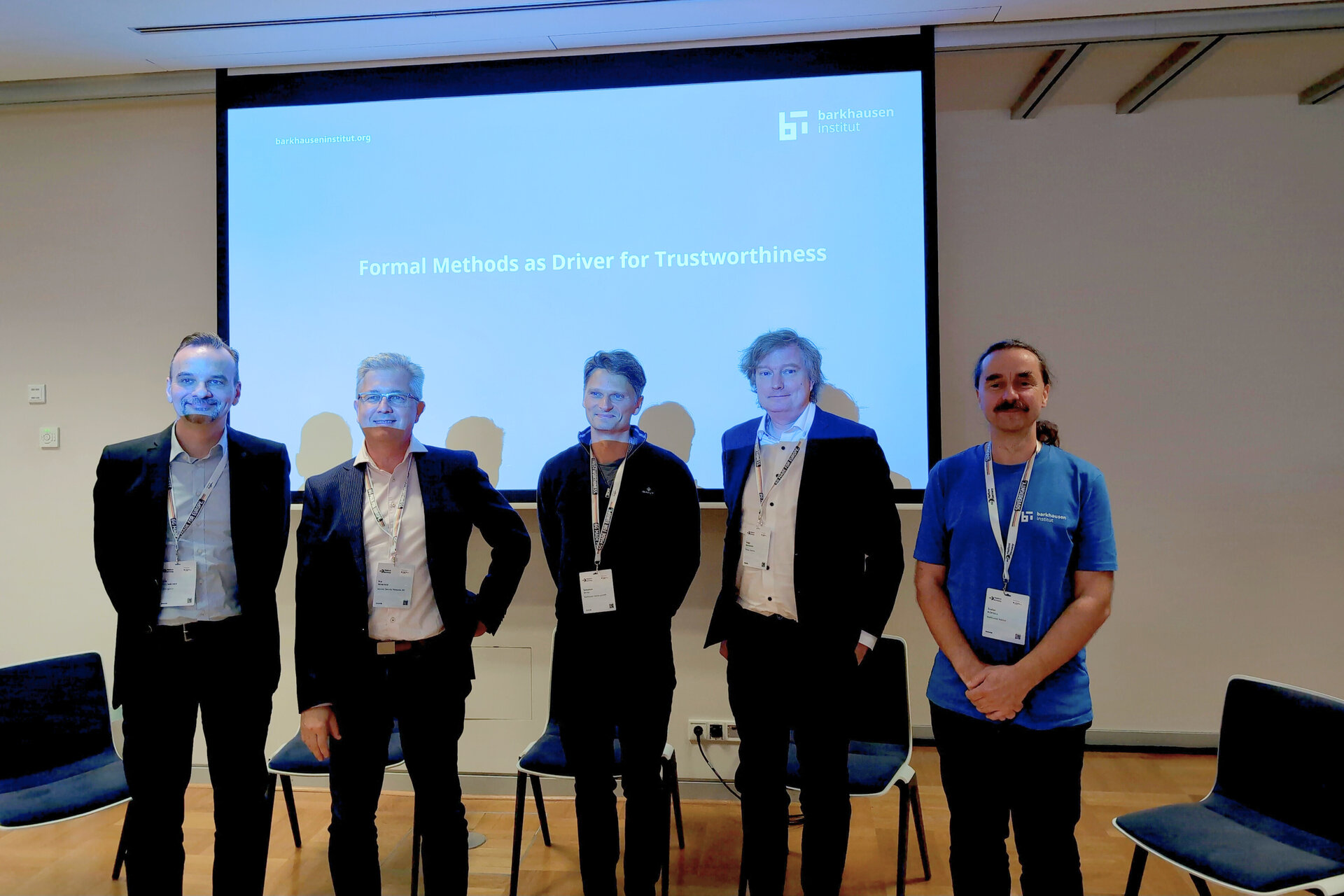 Five men standing in front of a presentation screen with the text 'Formal Methods as Driver for Trustworthiness'