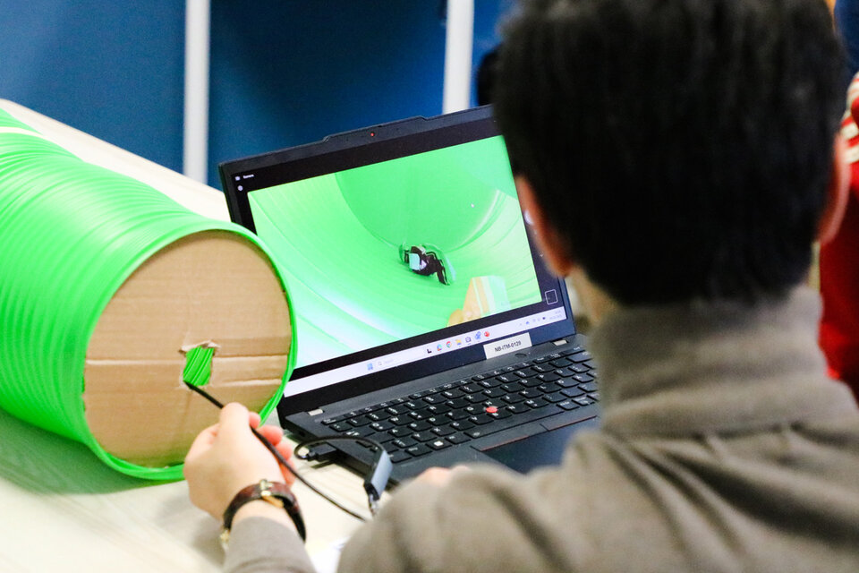 Person viewed from behind operates a small camera inside a green tube using a laptop. Focus on technology, experimentation, and exploration.