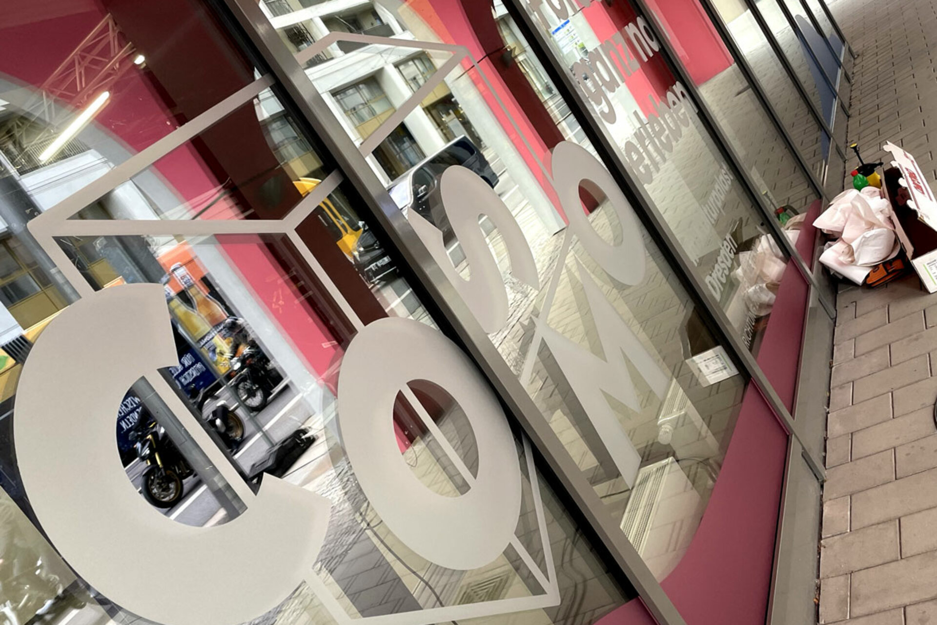 Große weiße Buchstaben 'COSMO' auf Glasfenster der Labore und Werkstatt des Barkhausen Instituts mit pinkfarbenen Hintergrund und Gehweg davor.
