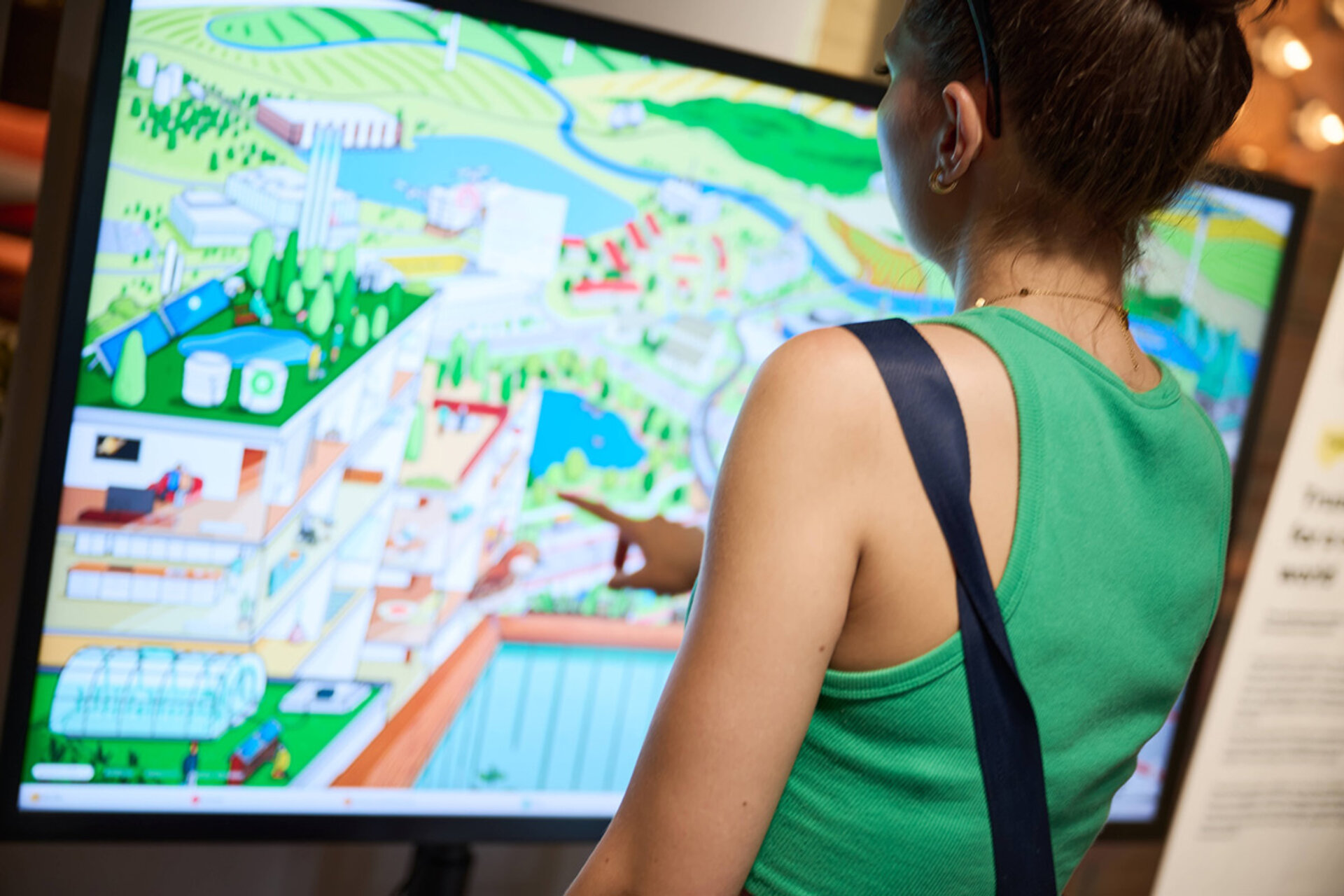 Frau mit grünem Oberteil zeigt auf eine bunte digitale Karte auf einem großen Bildschirm.