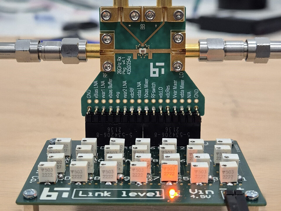 JCAS- Receiver PCB mit Supply Board mit Anschlüssen, beschrifteten Pins und einer orangefarbenen LED-Anzeige auf der Platine; außerdem das Logo des Barkhausen Instituts (BI)