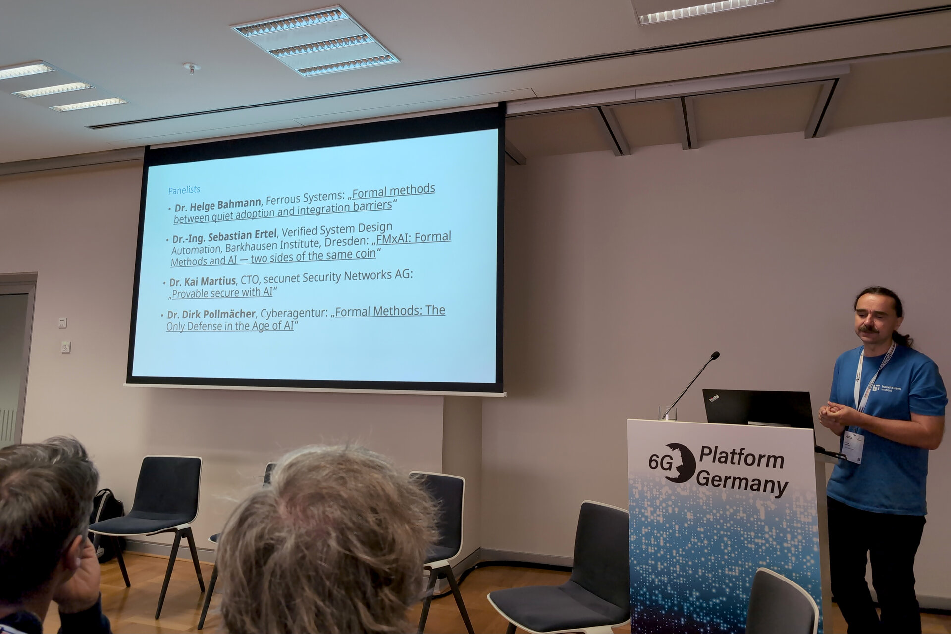 Man standing at a podium labeled '6G Platform Germany' giving a presentation with a slide listing speakers and topics related to formal methods in technology