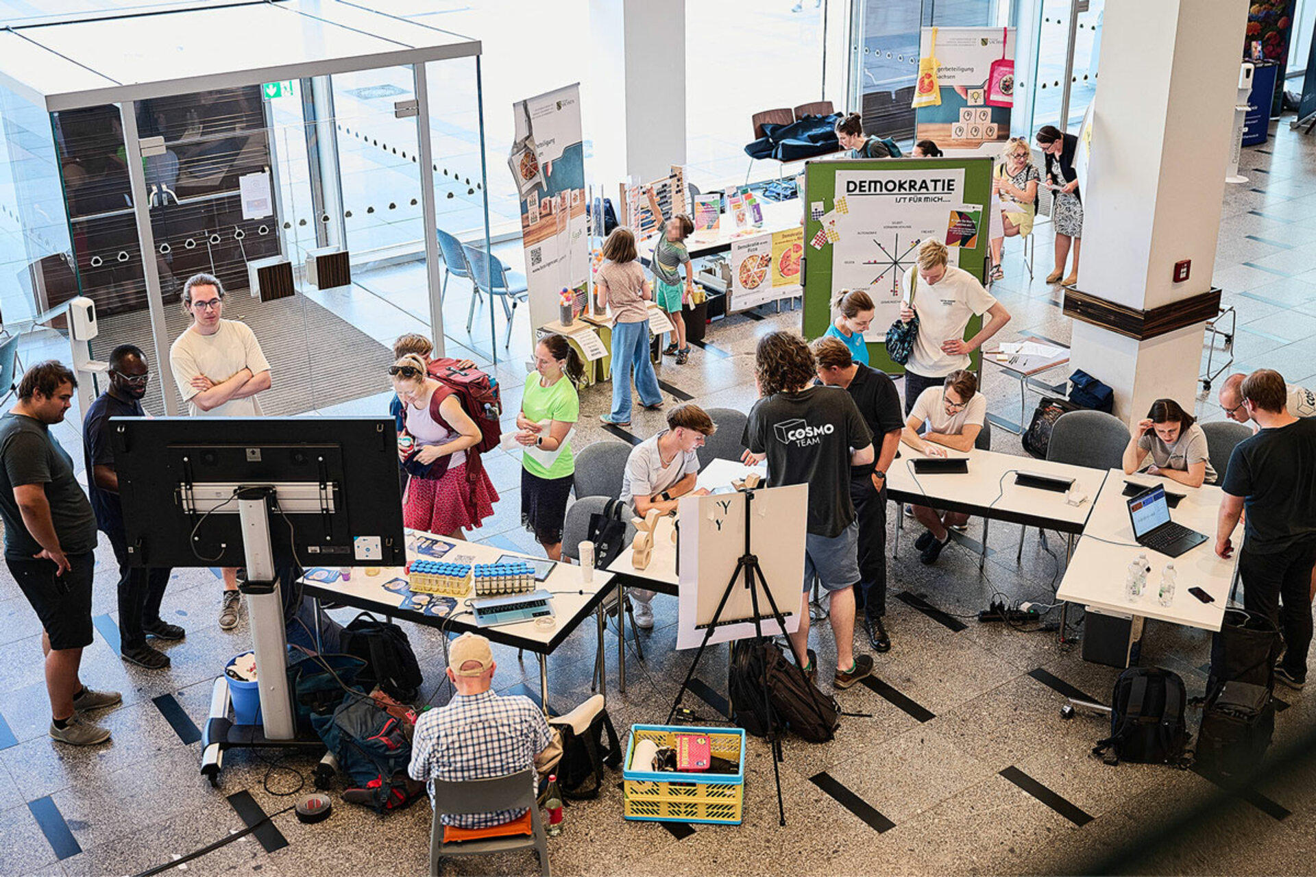 Mehrere Personen stehen und sitzen an Tischen mit Bildschirmen und Informationsmaterial in einem hellen Innenraum während der Lange Nacht der Wissenschaften Dresden 2026