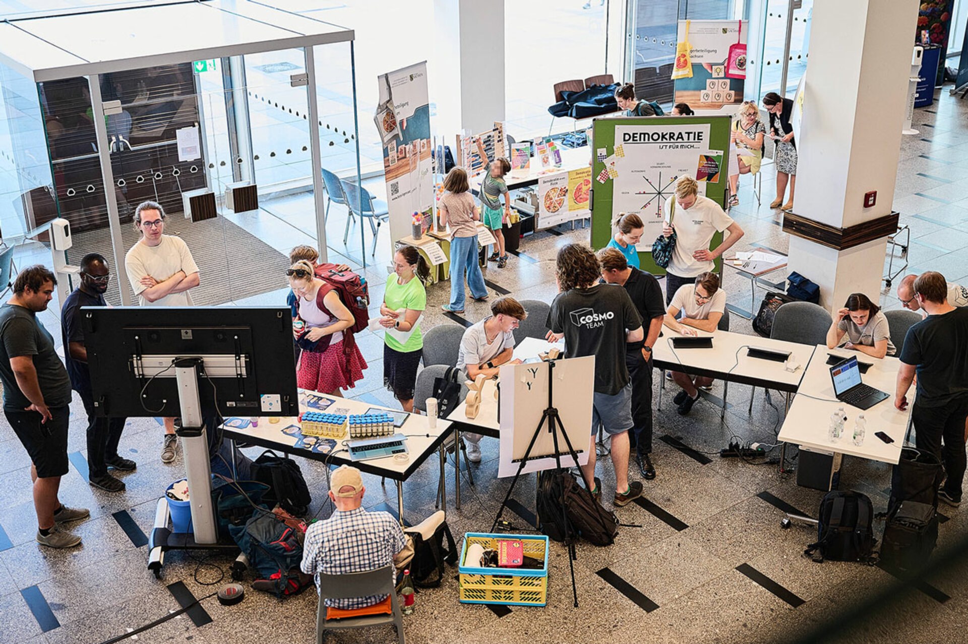 Mehrere Personen stehen und sitzen an Tischen mit Bildschirmen und Informationsmaterial in einem hellen Innenraum während der Lange Nacht der Wissenschaften Dresden 2026