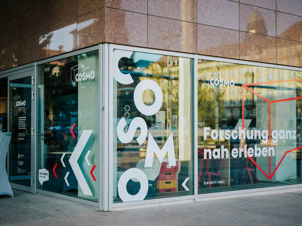 Exterior view of the COSMO Science Forum. The window reads “Experience research up close”