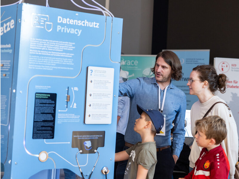 Ein Mann erklärt einer Frau und zwei Kindern an einem blauen Informationsstand mit dem Titel 'Datenschutz Privacy' im Barkhausen Institut beim Offenen Regierungsviertel 2026.