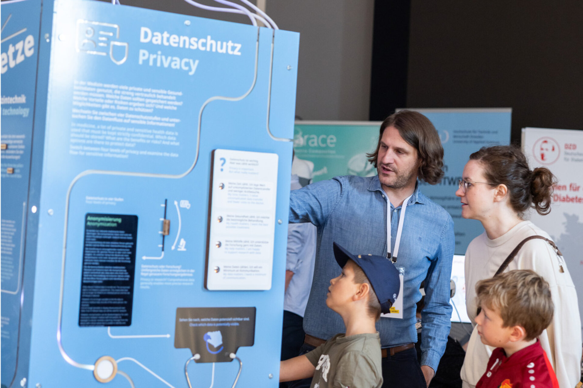 Ein Mann erklärt einer Frau und zwei Kindern an einem blauen Informationsstand mit dem Titel 'Datenschutz Privacy' im Barkhausen Institut beim Offenen Regierungsviertel 2026.