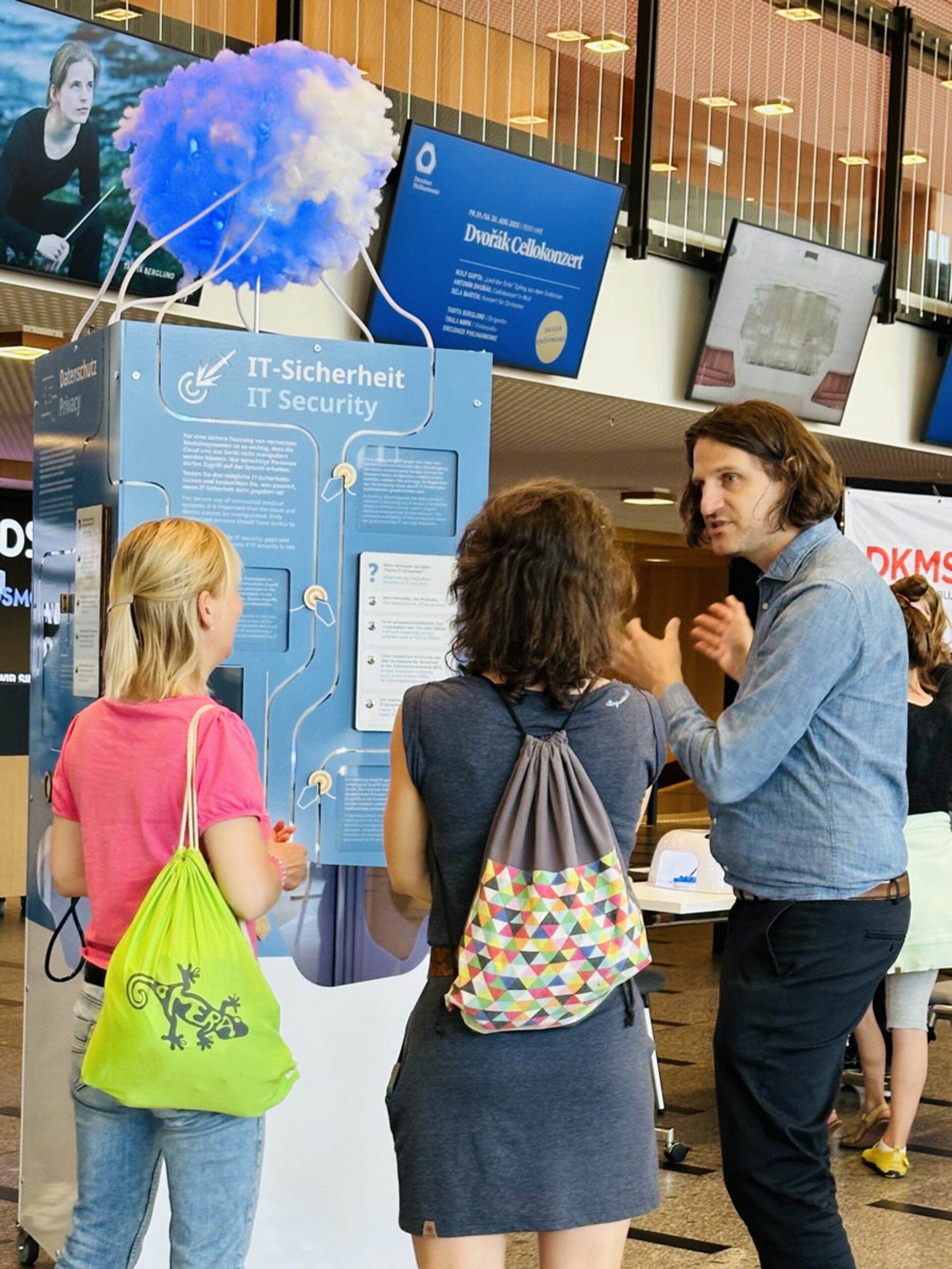 Ein Mann erklärt zwei Frauen im Foyer des Kulturpalastes Dresden ein Ausstellungsstück des Barkhausen Instituts zum Thema Datensicherheit. Die Ausstellung zeigt ein großes blaues Wolkenmodell. Spannende, lehrreiche Umgebung.