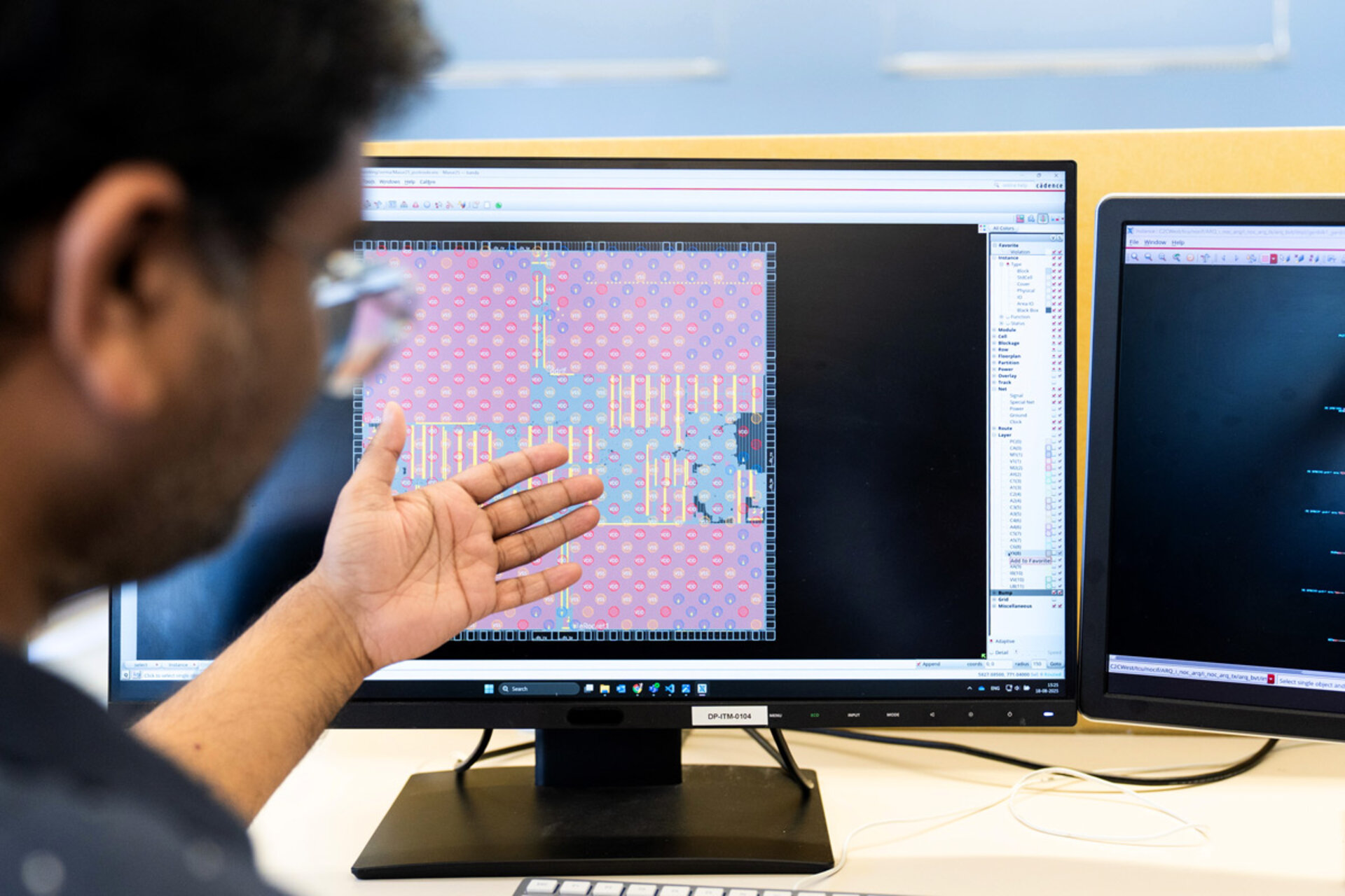 Person zeigt mit der Hand auf einen Monitor mit einer technischen Schaltplan- oder Leiterplattenansicht
