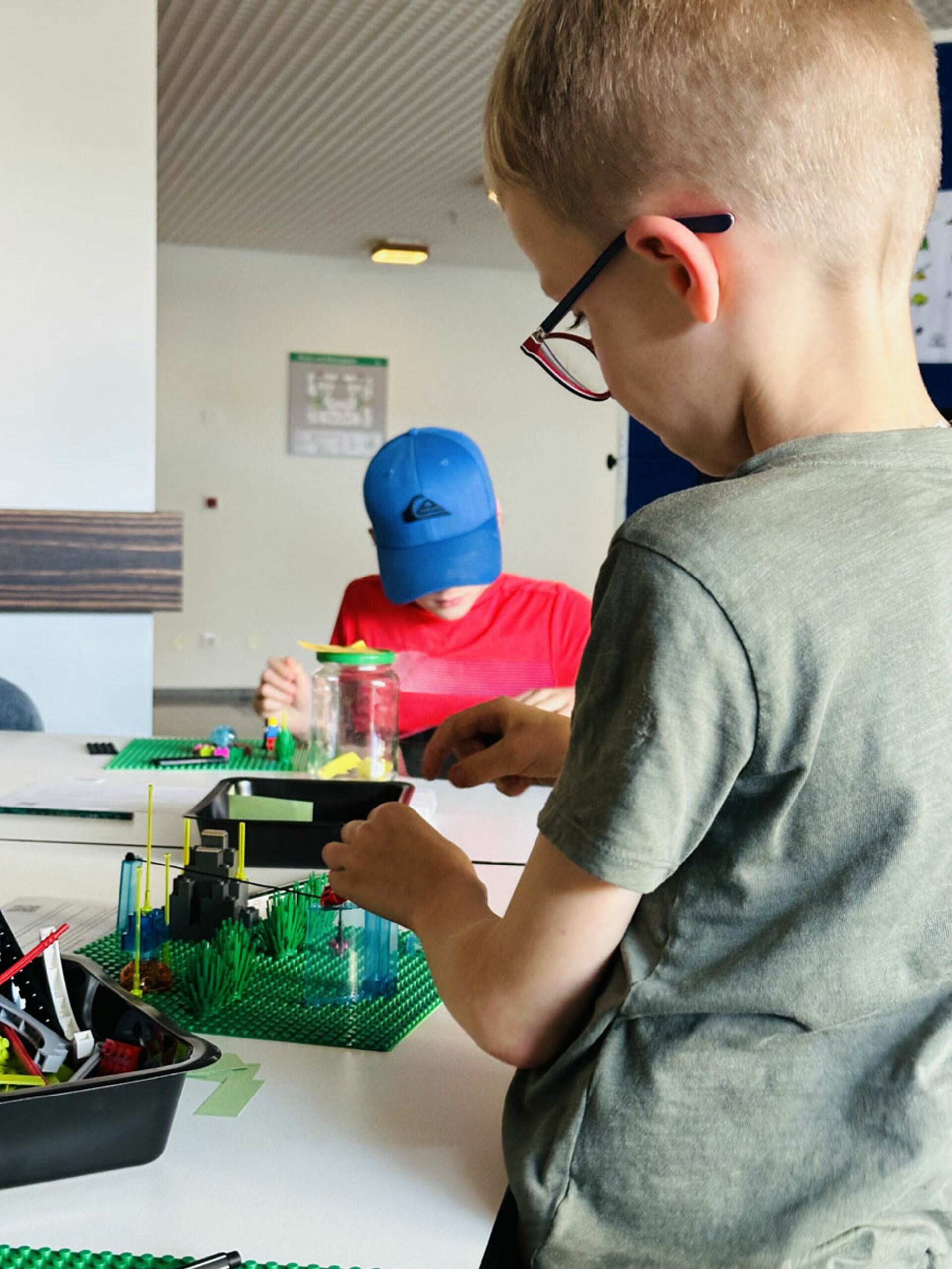 Kleine Kinder konzentrieren sich auf den Bau von LEGO Strukturen mit leuchtenden Farben und kreativen Teilen an einem Tisch. Die Stimmung ist spielerisch und phantasievoll.