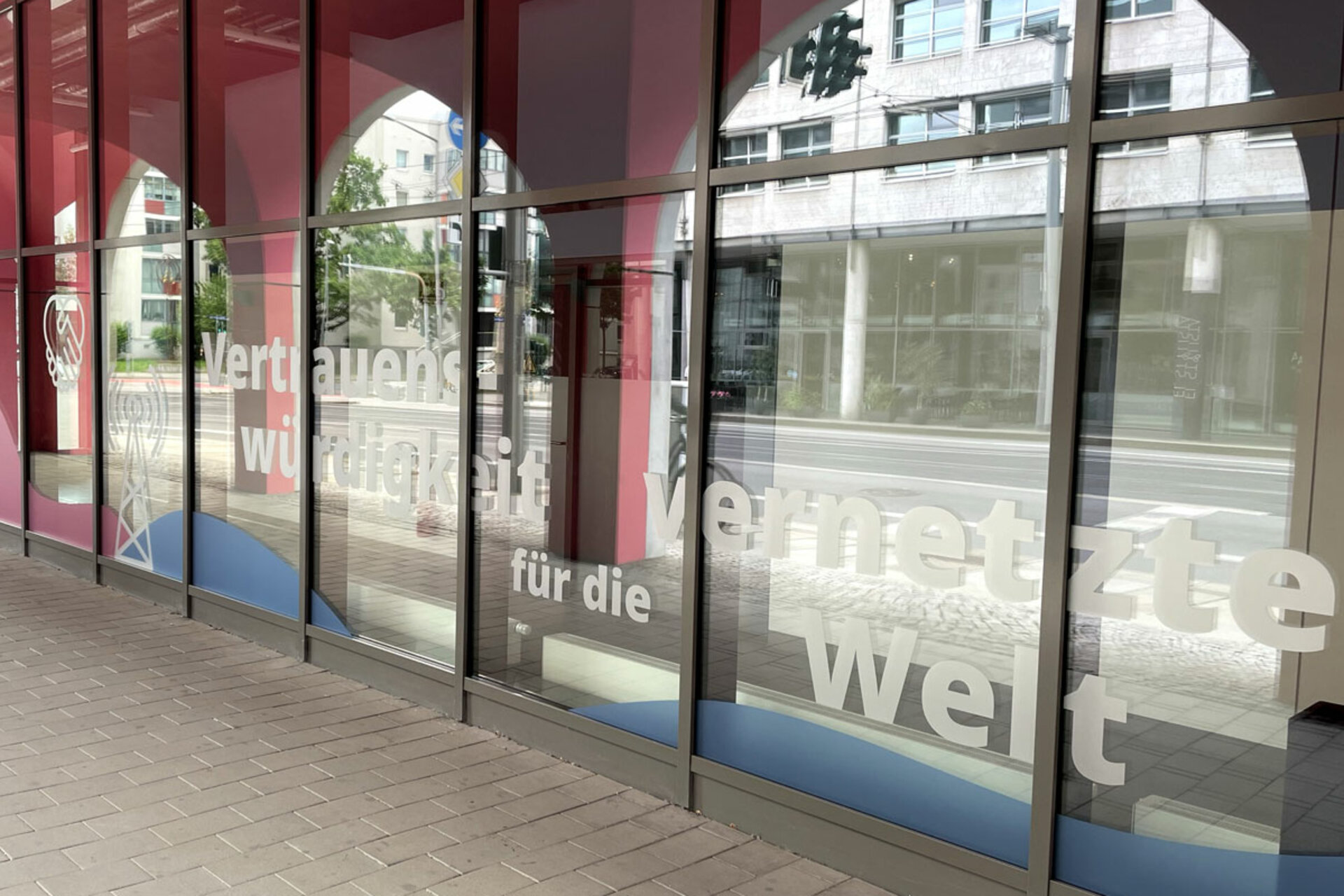 Große Glasfenster mit halbtransparentem Schriftzug 'Vertrauenswürdigkeit für die vernetzte Welt' in einem modernen Gebäude.