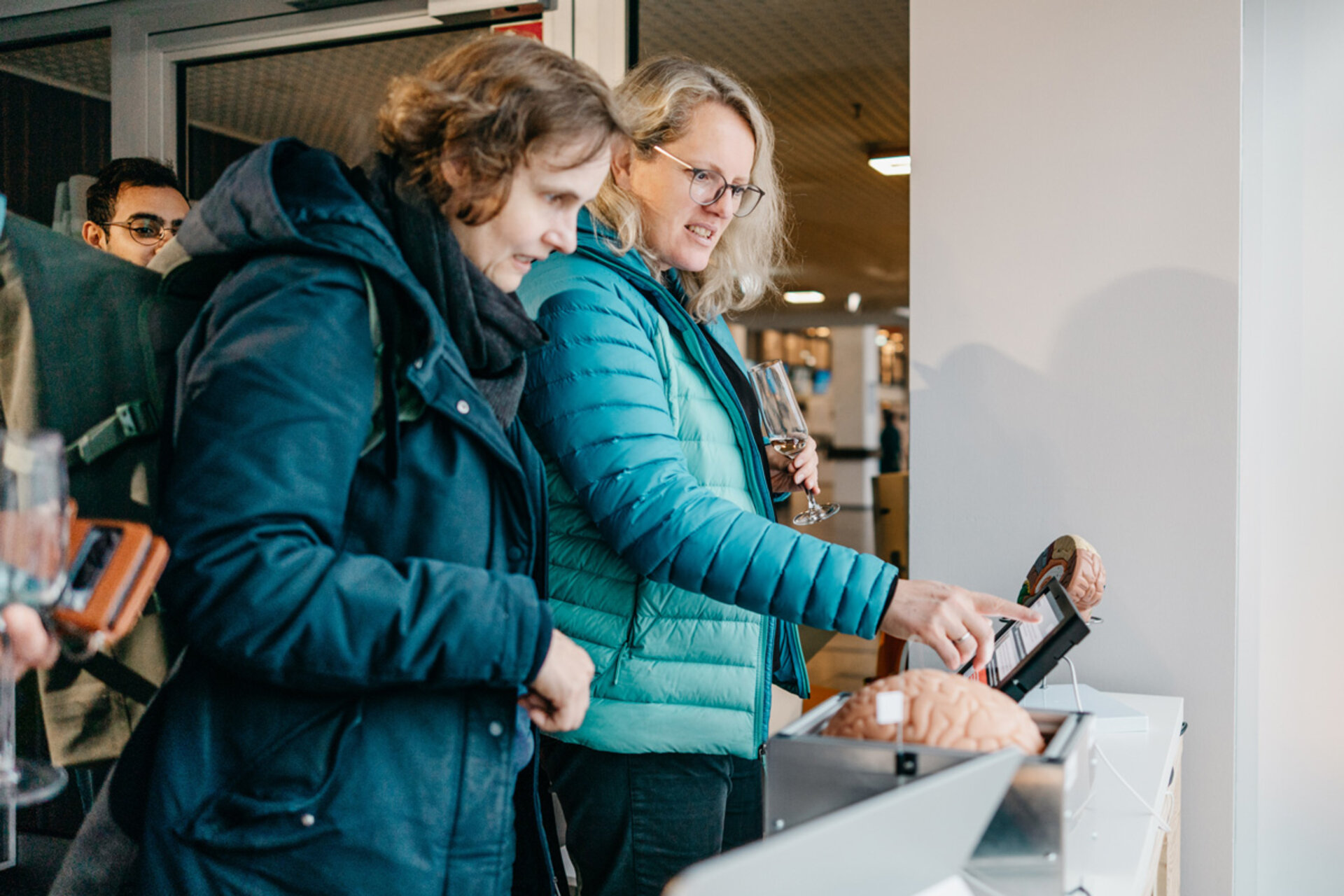 Zwei Frauen in Winterjacken bedienen interaktiven Bildschirm bei der Ausstellung „Mensch, Roboter! – Robotik aus der Dresdner Wissenschaft“.
