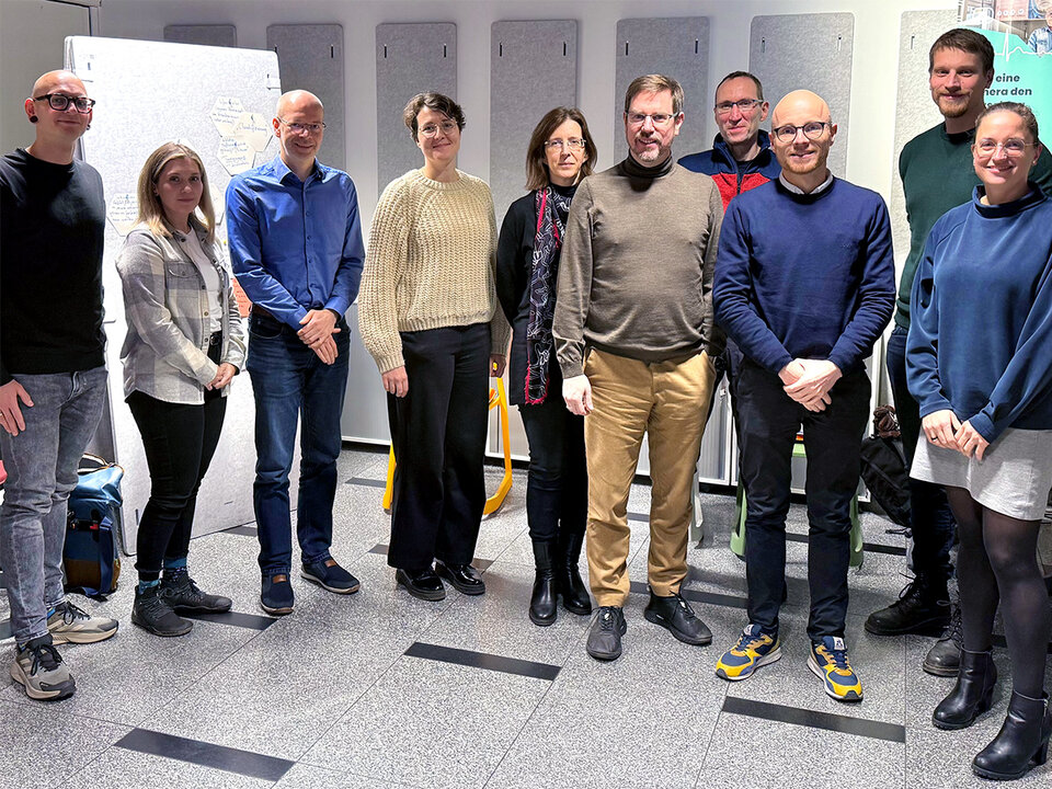 Group of ten people standing indoors on a tiled floor, dressed in casual and business casual clothing.
