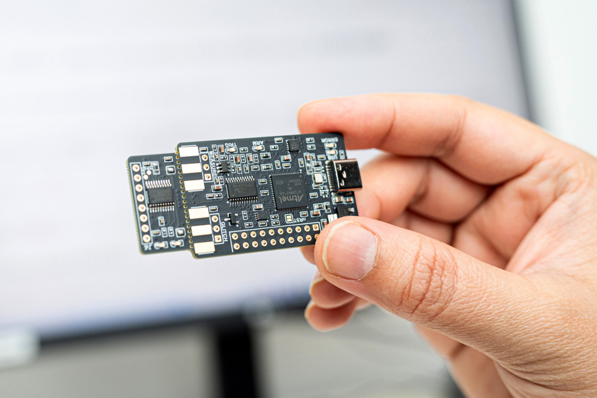Hand holding a small black printed circuit board with multiple electronic components and a USB connector