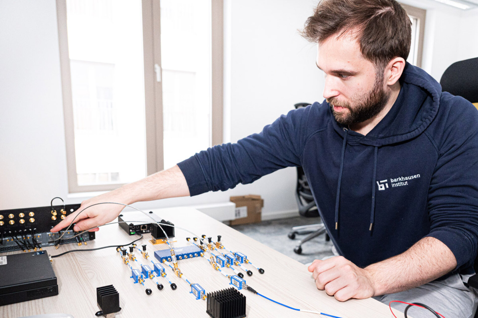 Person in Kapuzenpullover bedient elektronische Messgeräte auf einem Tisch in einem hellen Raum