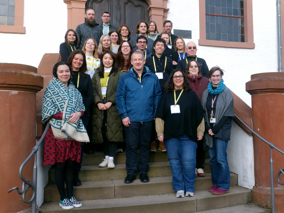 You see a group of people in front of an entrance area on a staircase. Most of them are smiling.
