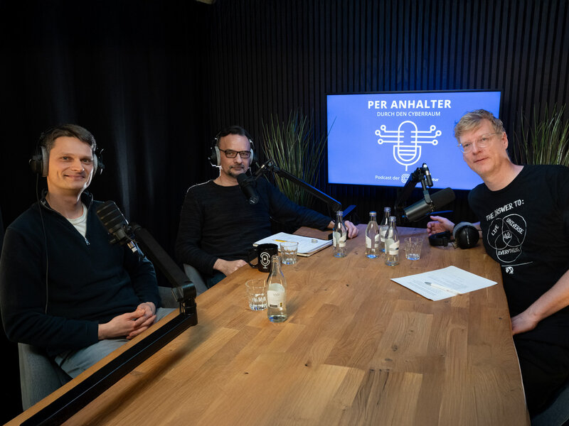 Drei Männer sitzen an einem Tisch mit Audiogeräten