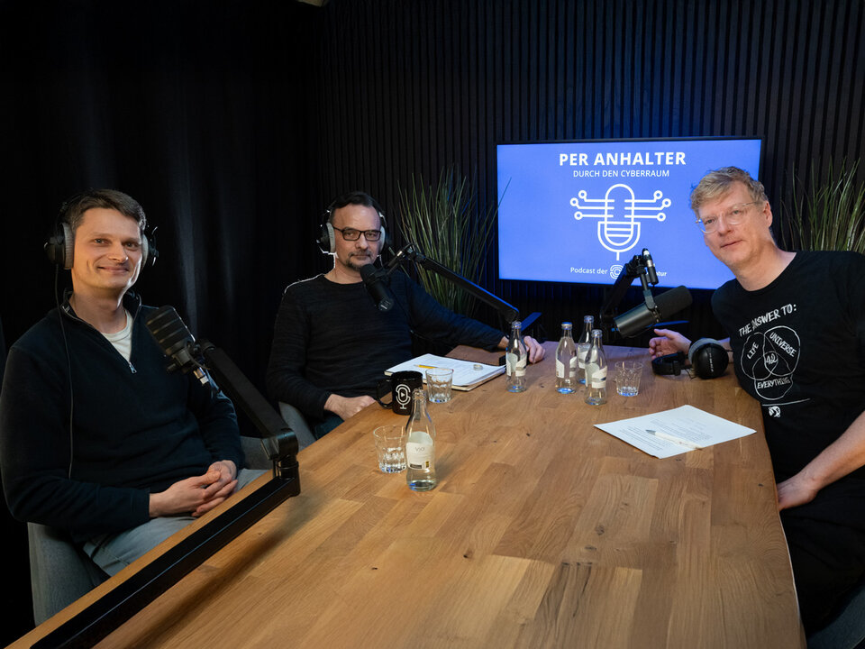 Drei Männer sitzen an einem Tisch mit Audiogeräten