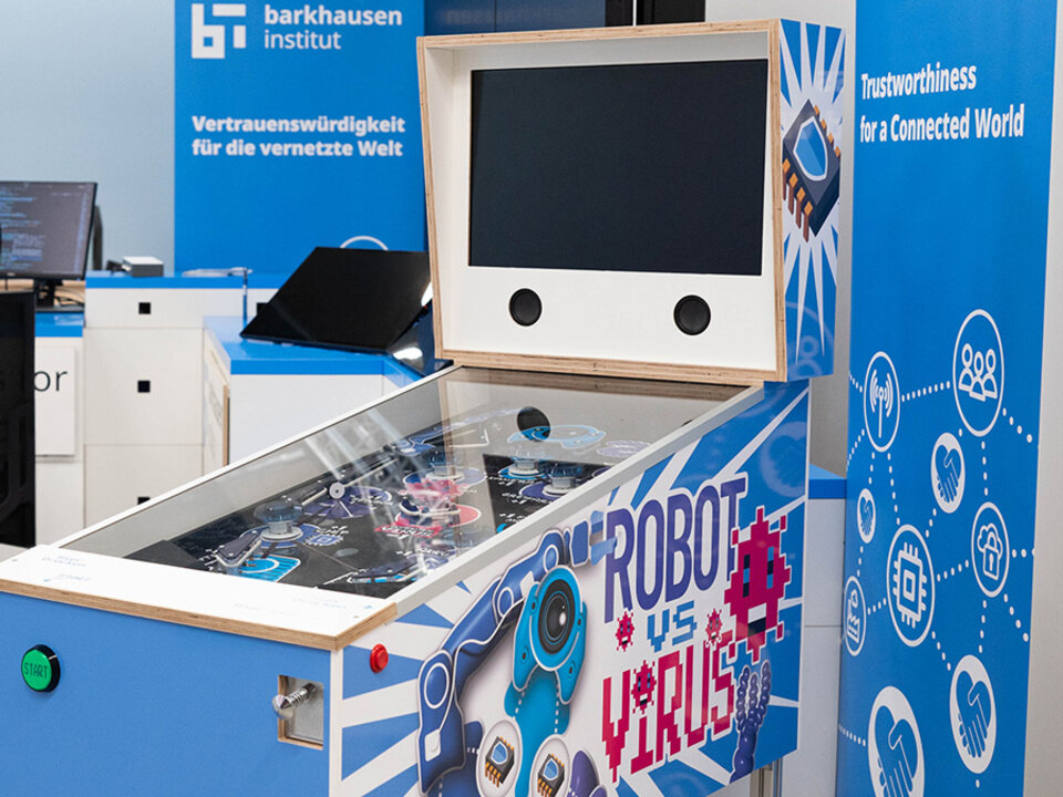 Pinball machine with a screen designed as a robot face and side panel text reading 'ROBOT vs VIRUS' in a blue exhibition booth