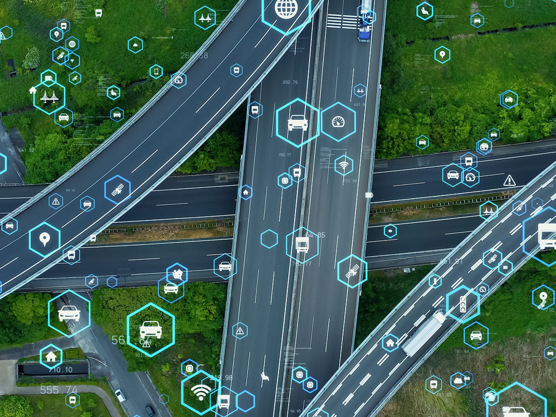 You have a bird's eye view of several streets lying on top of each other. Few cars drive on the roads. All around you are green meadows and green treetops. Symbols in light blue hexagons float above the streets. The symbols are from the 'traffic' theme, e.g. a car, a traffic light.