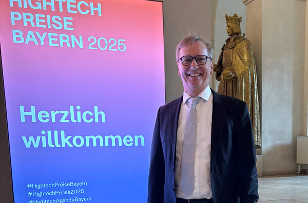 Gerhard Fettweis stands in the entrance area next to a sign with “Welcome” and “Hightech Preise Bayern 2025”