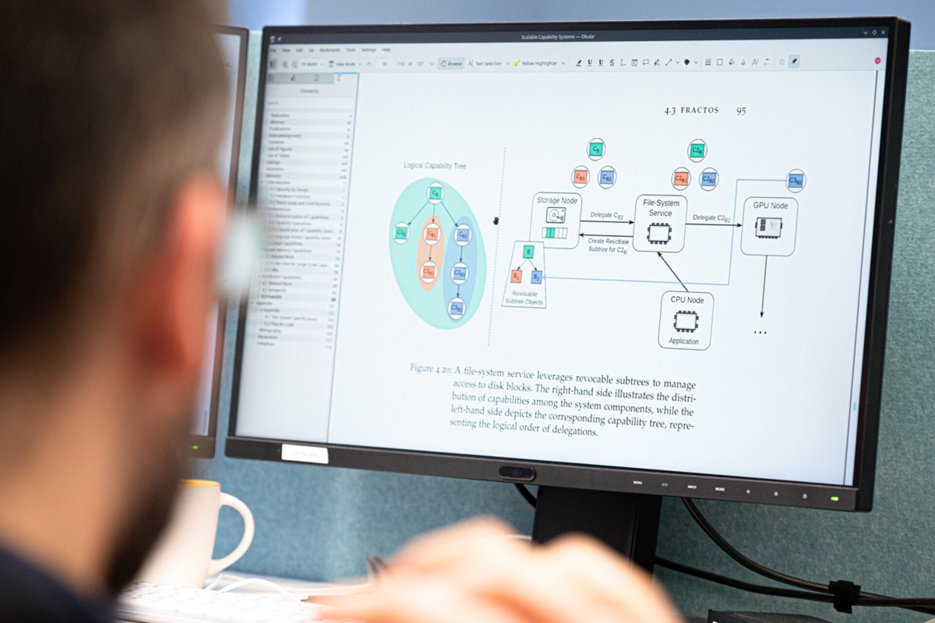 Ein unscharfer Vordergrund zeigt eine Person, die auf einen Computerbildschirm blickt. Auf dem Bildschirm ist eine Infografik mit mehreren farbigen Kästchen, Pfeilen und Verbindungslinien zu sehen. Rechts daneben befindet sich ein längerer Textabschnitt. Die Infografik stellt verschiedene Komponenten und deren Beziehungen dar. Die Benutzeroberfläche des Programms ist hell und zeigt Menüs und Werkzeugleisten am oberen Rand.