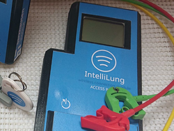 Es sind 3 blaue Geräte zu sehen mit jeweils einem Bildschirm. Darauf steht 'IntelliLung' und die Funktion des gerätes. Außerdem sieht man 3 farbige Kabel in grün, rot und gelb, mit Klemme am Ende.