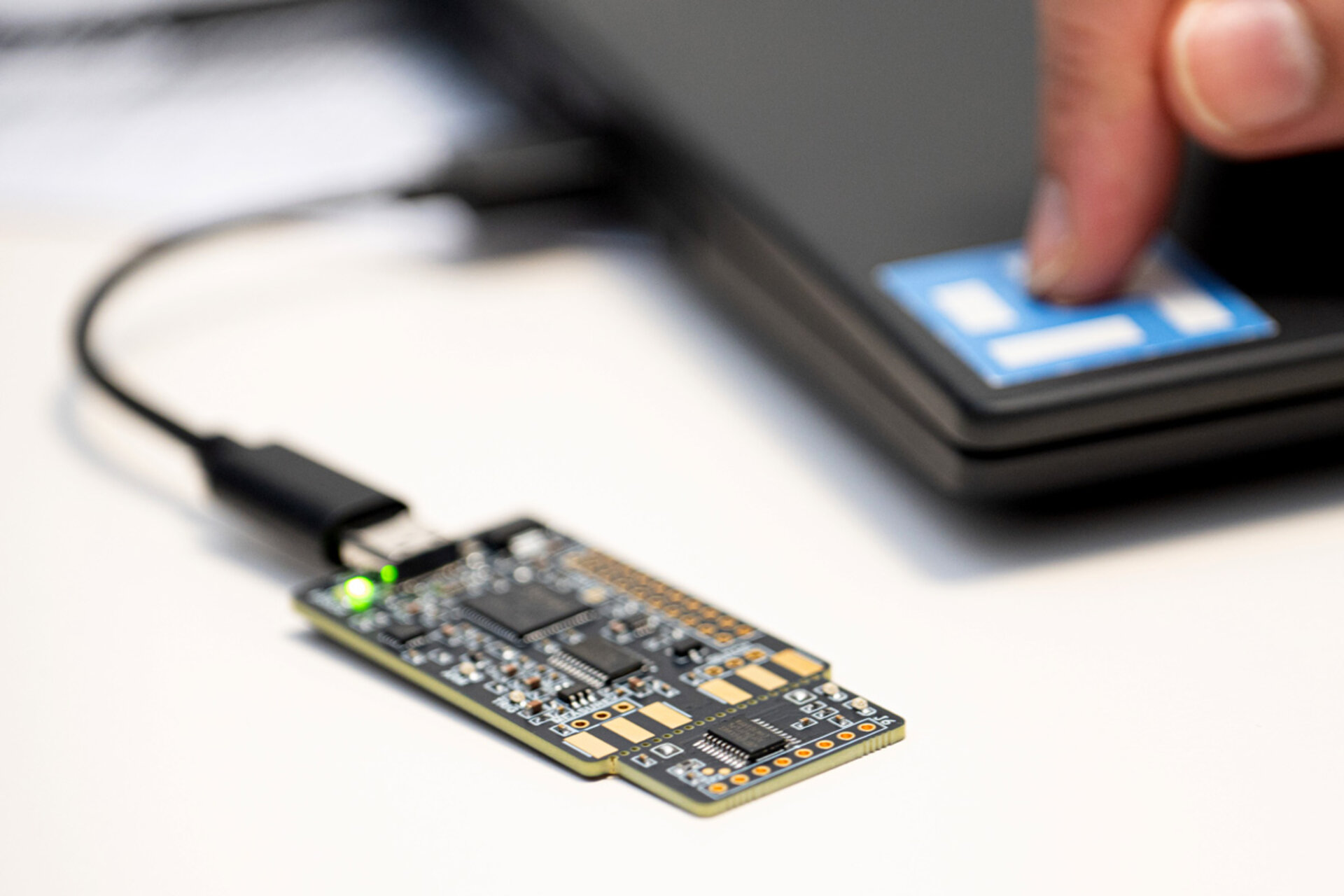 Close-up of a circuit board connected by a cable to a laptop keyboard with a finger pressing a key