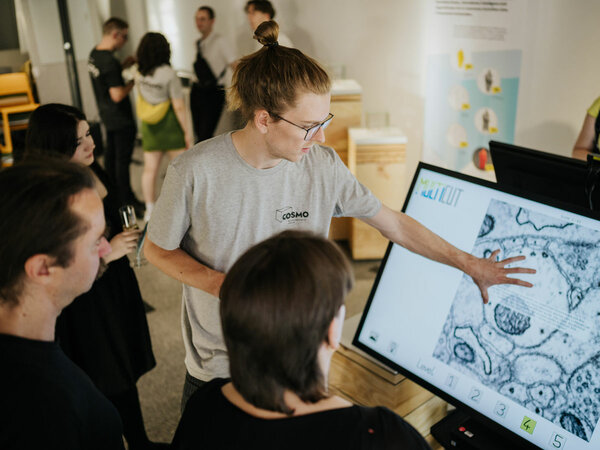 An employee of the COMSO Science Forum explains the image on a monitor to a group of guests