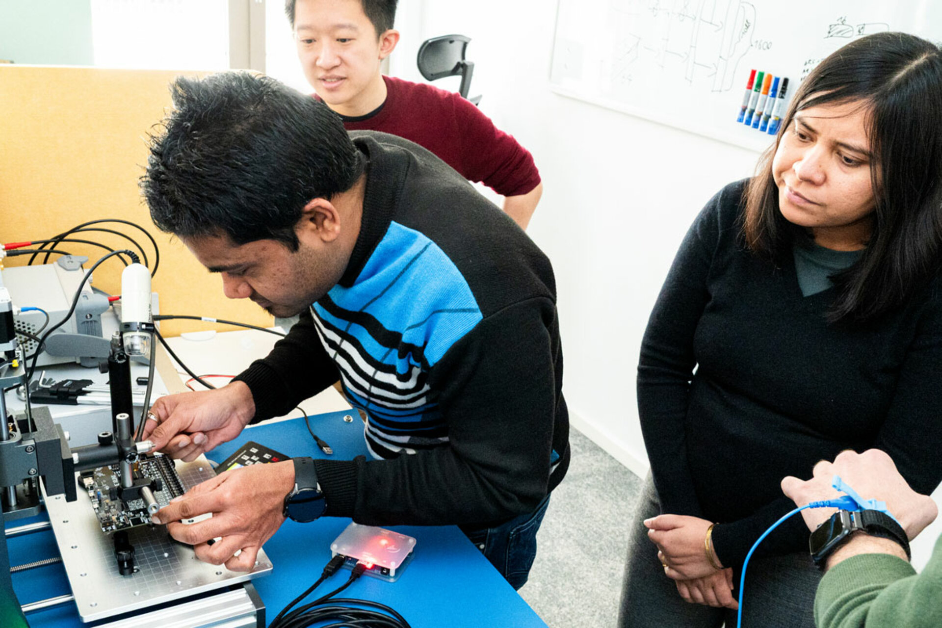 Three people working with electronic equipment on a blue table in a lab setting