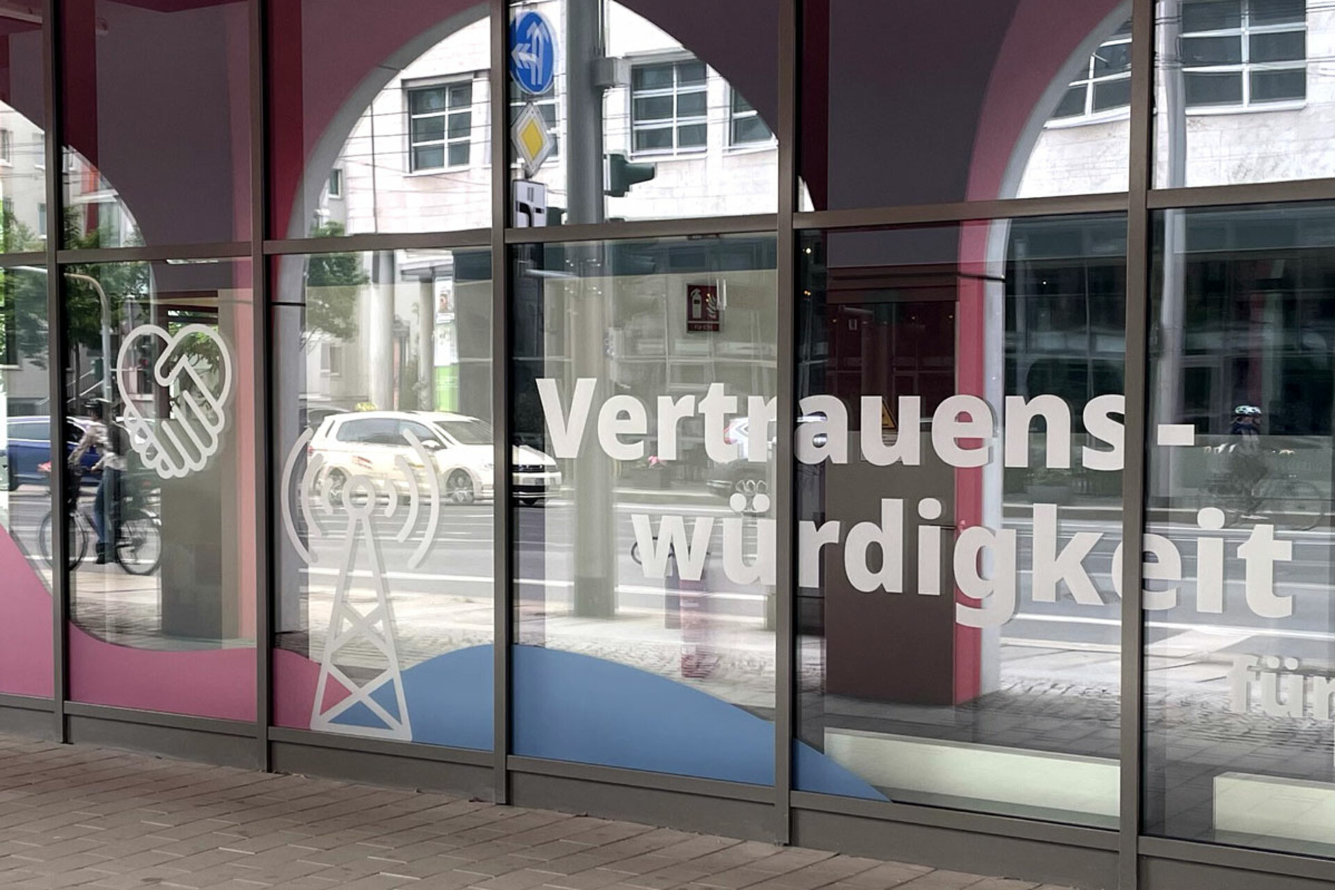 Fensterscheiben mit dem Wort 'Vertrauenswürdigkeit' und Symbolen für Handschlag und Funkmast.