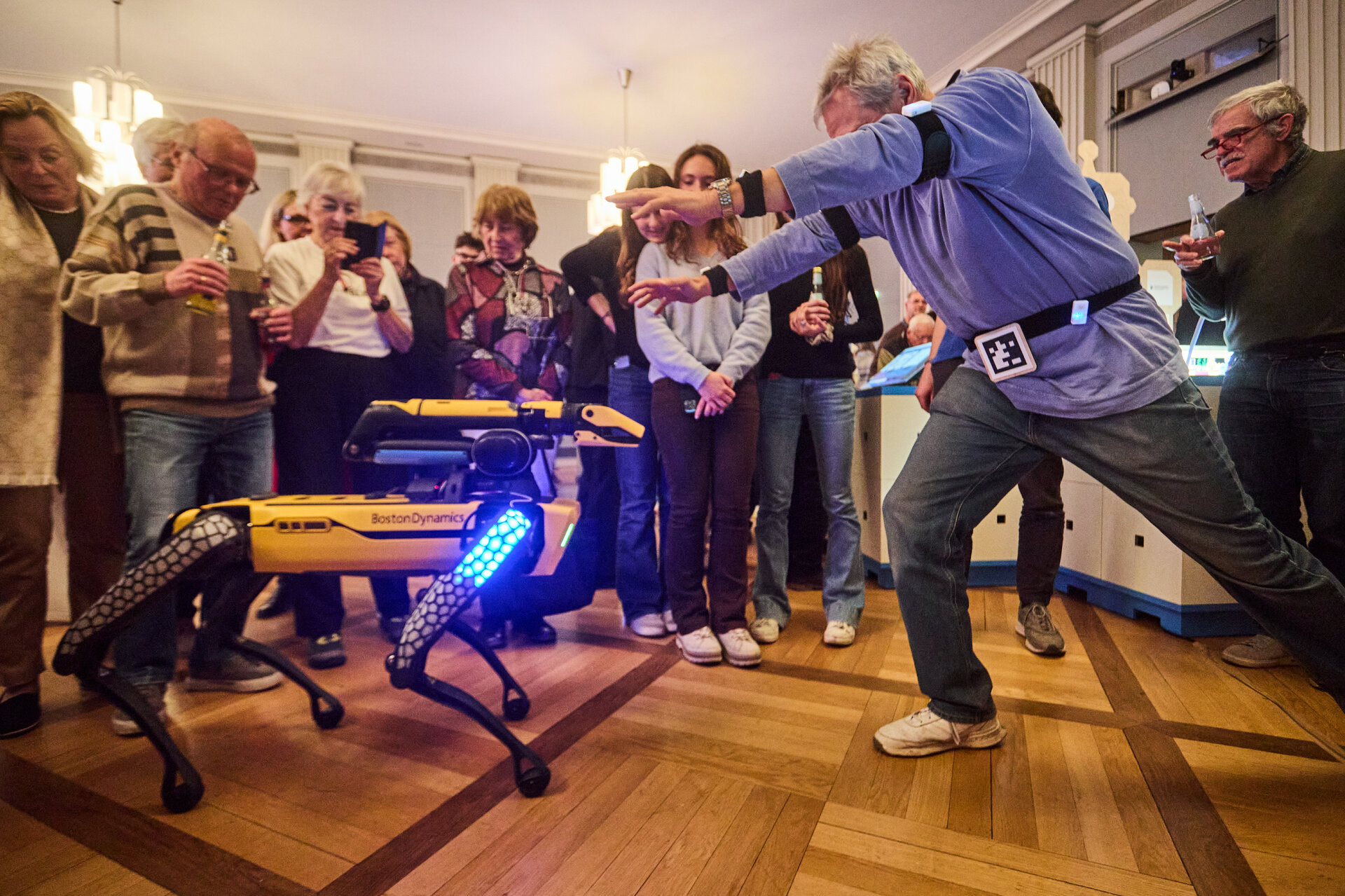 Group of people watching a person interacting with a four-legged robot with blue lights indoors