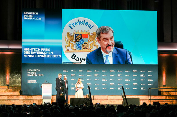 You see a stage with a few people in the background and a big screen with Markus Söder.