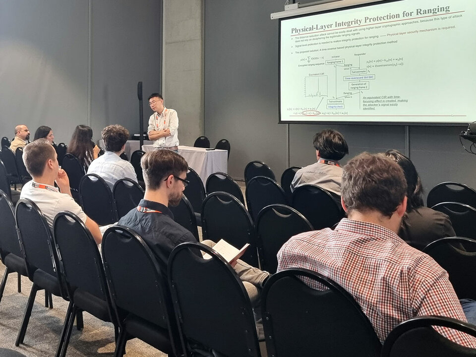 A speaker presents during the workshop "Enabling Security, Trust, and Privacy in 6G Wireless Systems" at IEEE GLOBECOM 2024. The slide focuses on physical-layer integrity protection for ranging. Several attendees are visible in the audience.