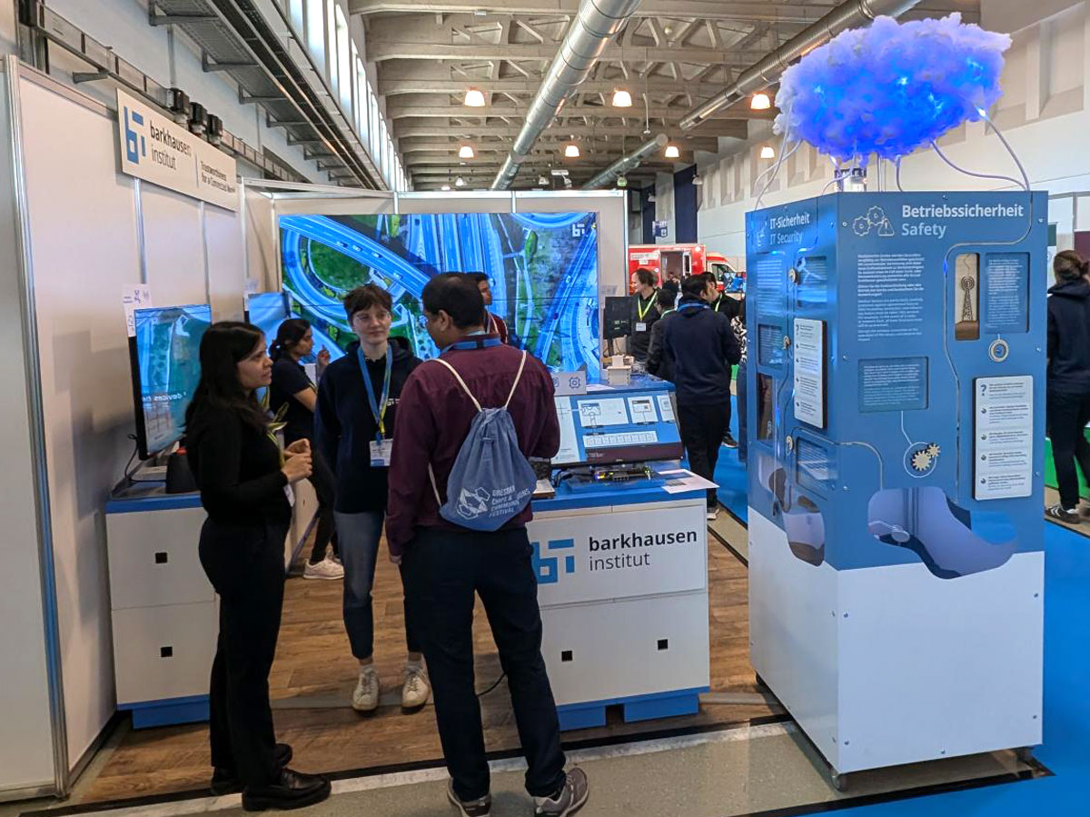 Messestand des Barkhausen Instituts mit interaktiver Ausstellung zu Betriebssicherheit und mehreren Besuchern im Gespräch.